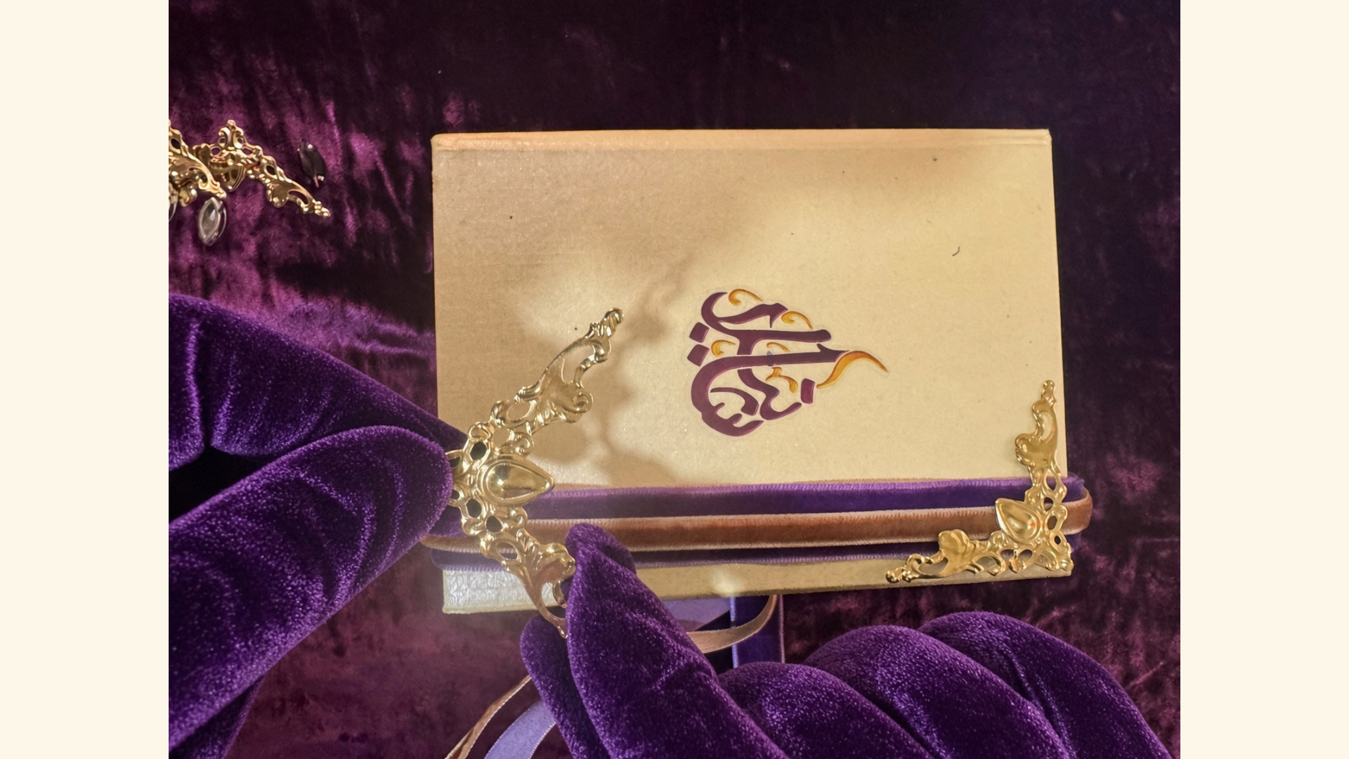 Purple-gloved hands applying an ornate gold corner to a House of Shaneela presentation box.
